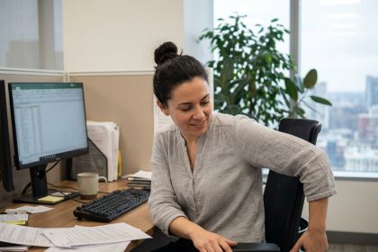Femme ajustant la hauteur de sa chaise de bureau ergonomique dans un open space moderne pour prévenir les troubles musculo-squelettiques